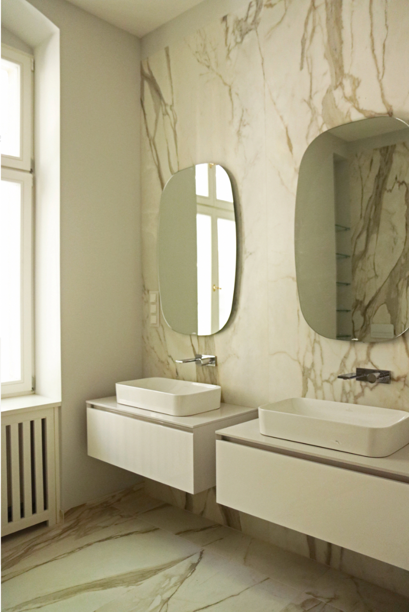 Artprojekt Interior Design Altbau Ku'damm bathroom white sinks with a marble background and two squarish round mirrors.