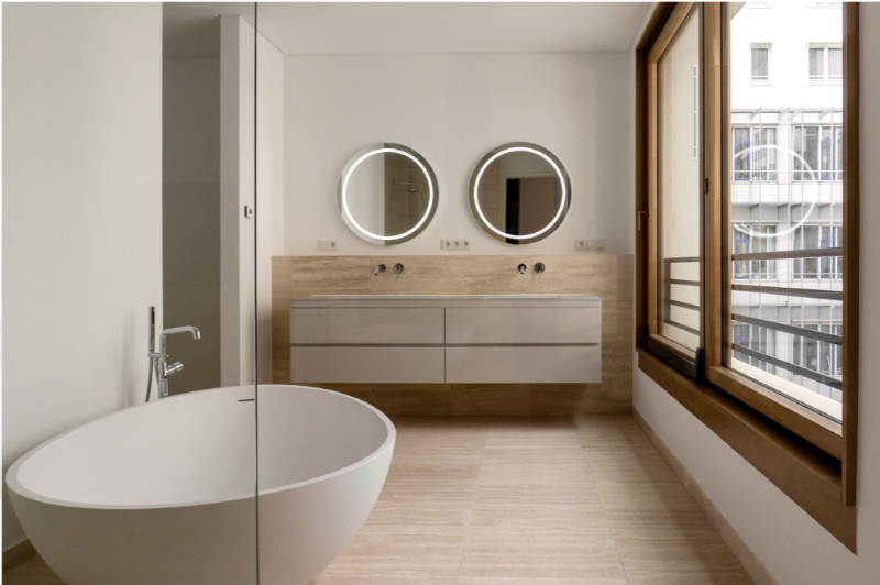 Artprojekt Interior Design Modern Apartment Palais Varnhagen bathroom, the image features a big white oval bathtub. A tap coming from the floor into the bathtub. Two round mirrors and a cabinet on a wooden background.
