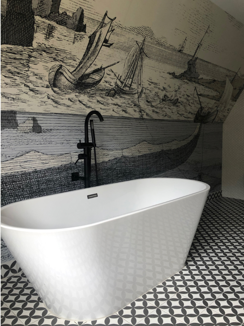Artprojekt Interior Design Mid Century Villa bathroom with a unique wall, showing us ships sailing on the ocean. A White bathtub with a black, more classic tab.