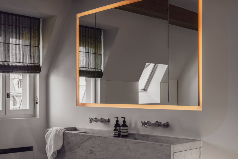 Bathroom Decor from Hélène Van Marcke. Marble washbasin and minimalist miroir with leds. We can see the traditional parisian apartment from the window