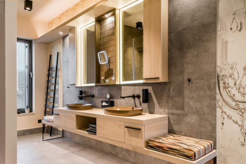 Elternbad-Interiordesign with industrial grey tile, a costumedame washbasin in light wood with yellow mustard sinks. 2 big mirrors and a little sitting area connected to the washbasin.