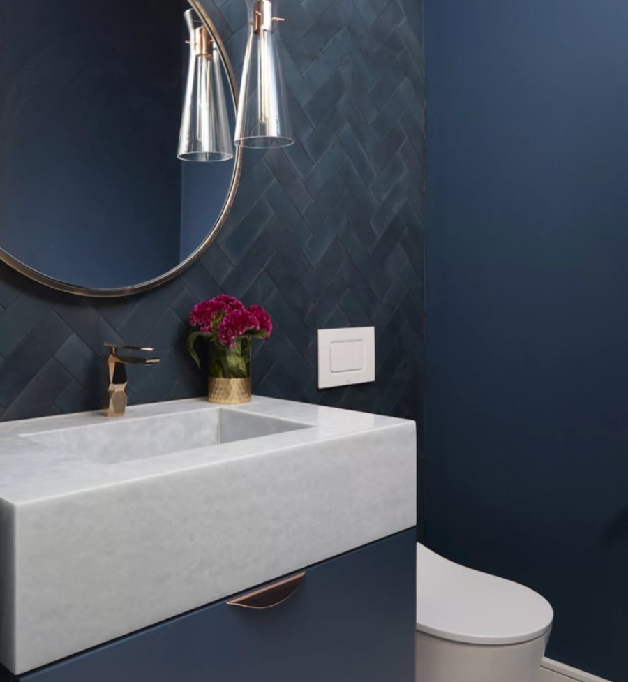Bathroom designs ideas by Dvira Interiors. For the vanity and countertop, they used a white stone and picked a blue cabinet colour for the vanity cabinets. They applied blue textured herringbone tiles along the accent wall for a stylish effect!