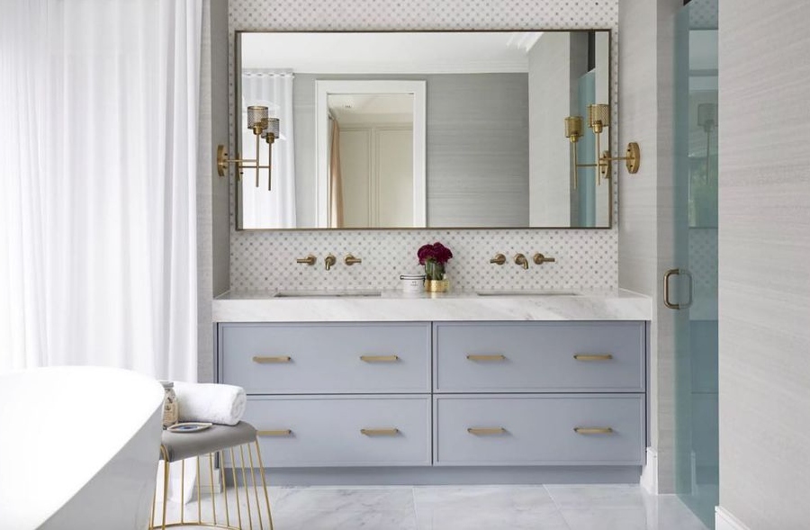 Bathroom designs ideas by Dvira Interiors.This spacious master bathroom feels bright with an all-white palette, accented with a sculptural bathtub and stylish custom double vanity in blue with a countertop in marble. The bathroom has a lot of golden details.