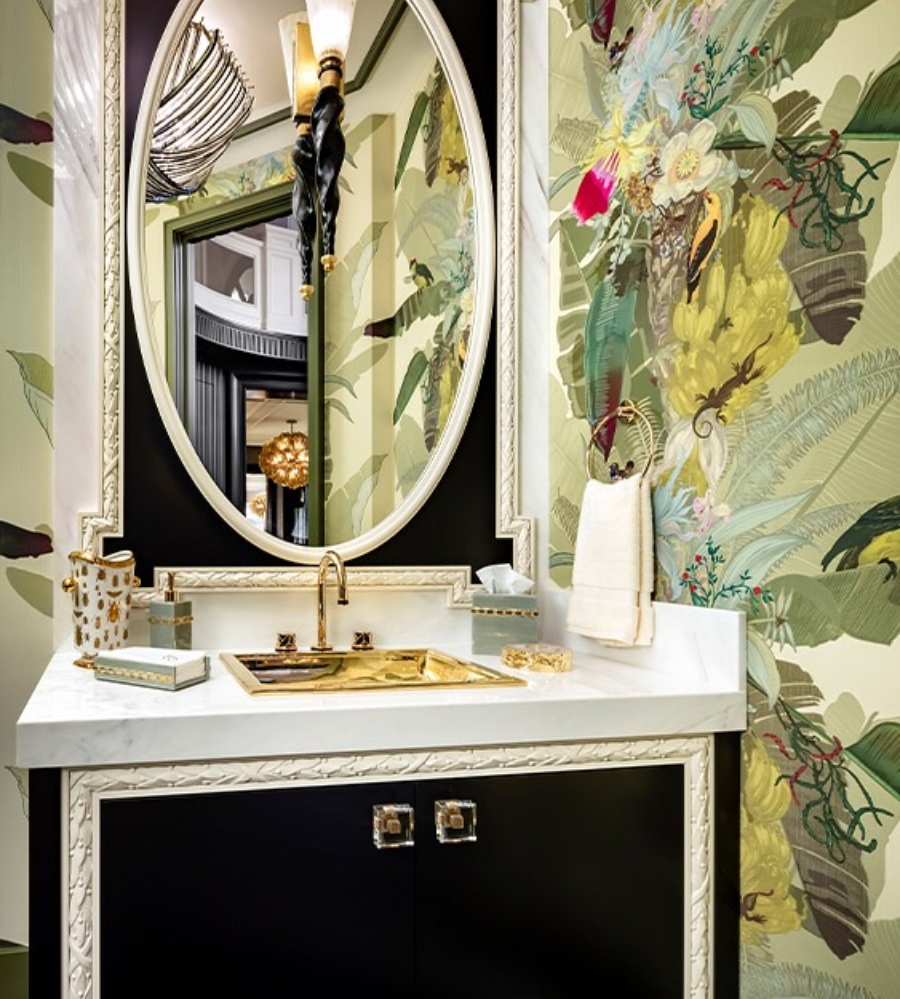 Luxury bathroom by Lori Morris Design. This bathroom has wallpaper in green with plants and flowers, a black and white mirror, and a black vanity with a white countertop.