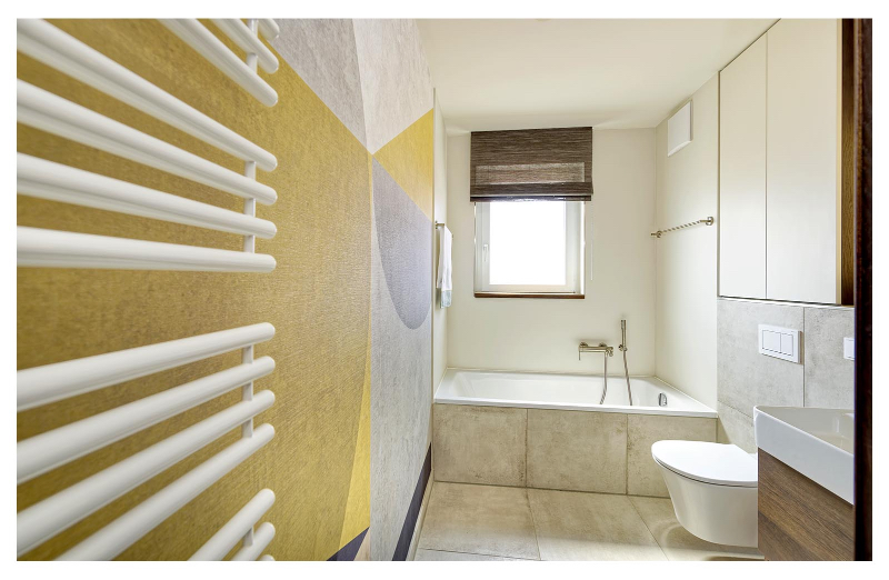 Heerwagen- Design Consulting TERRASSENWOHNUNG NEUPASING bathroom. Here we see the bathtub and a square mirror, with a wall painted in yellow and blue tones.