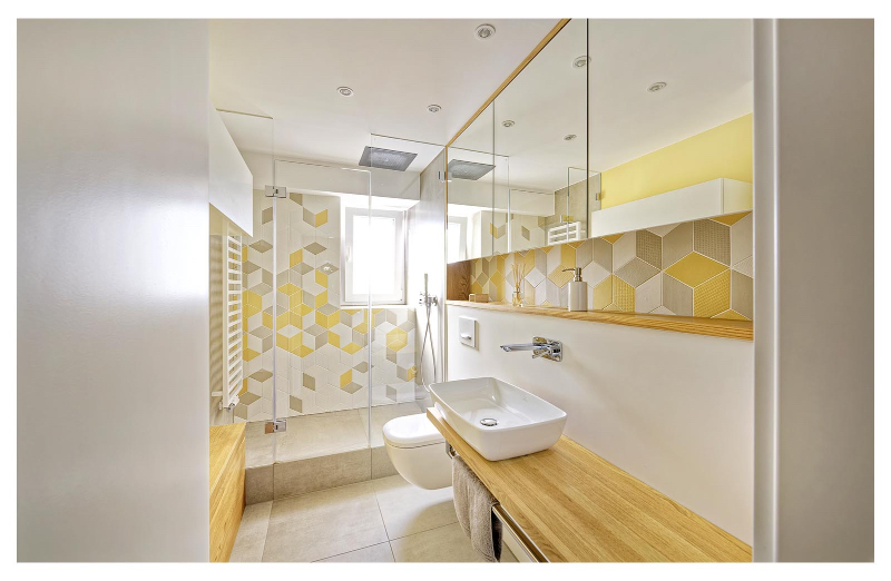 Heerwagen- Design Consulting AUS 2 MACH 1. The bathroom is composed of yellow, grey and white tones. Here we see a walk in shower, a toilet and and a washbasin.