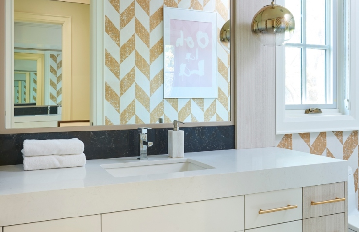 Bathroom design ideas from Stacey Cohen Design. This modern bathroom has white and yellow wallpaper, a gold suspension lamp, a mirror, and white vanity with gold details.
