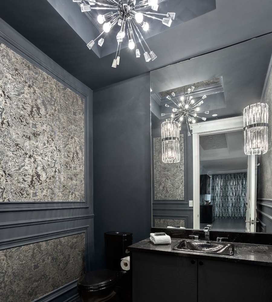 Ideas to decorate the bathroom by Beyond Beige. This dark bathroom has blue and grey walls with a black cabinet and countertop and two luxurious chandeliers.