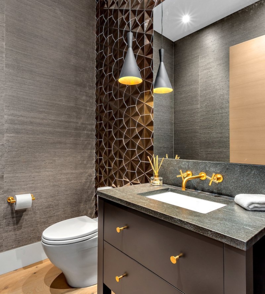 Ideas to decorate the bathroom by Beyond Beige. This dark bathroom has one brown wall, a brown cabinet with a grey countertop, and golden features.