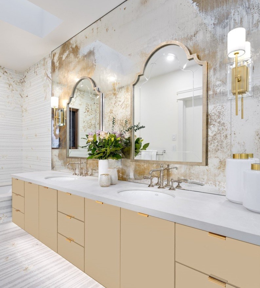 Ideas to decorate the bathroom by Beyond Beige. This master bathroom with white and gold walls has a gold cabinet with a white marble countertop and golden mirrors.